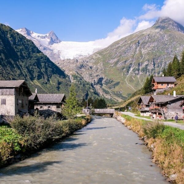 Village alpin traditionnel au bord d’un torrent, face à un glacier